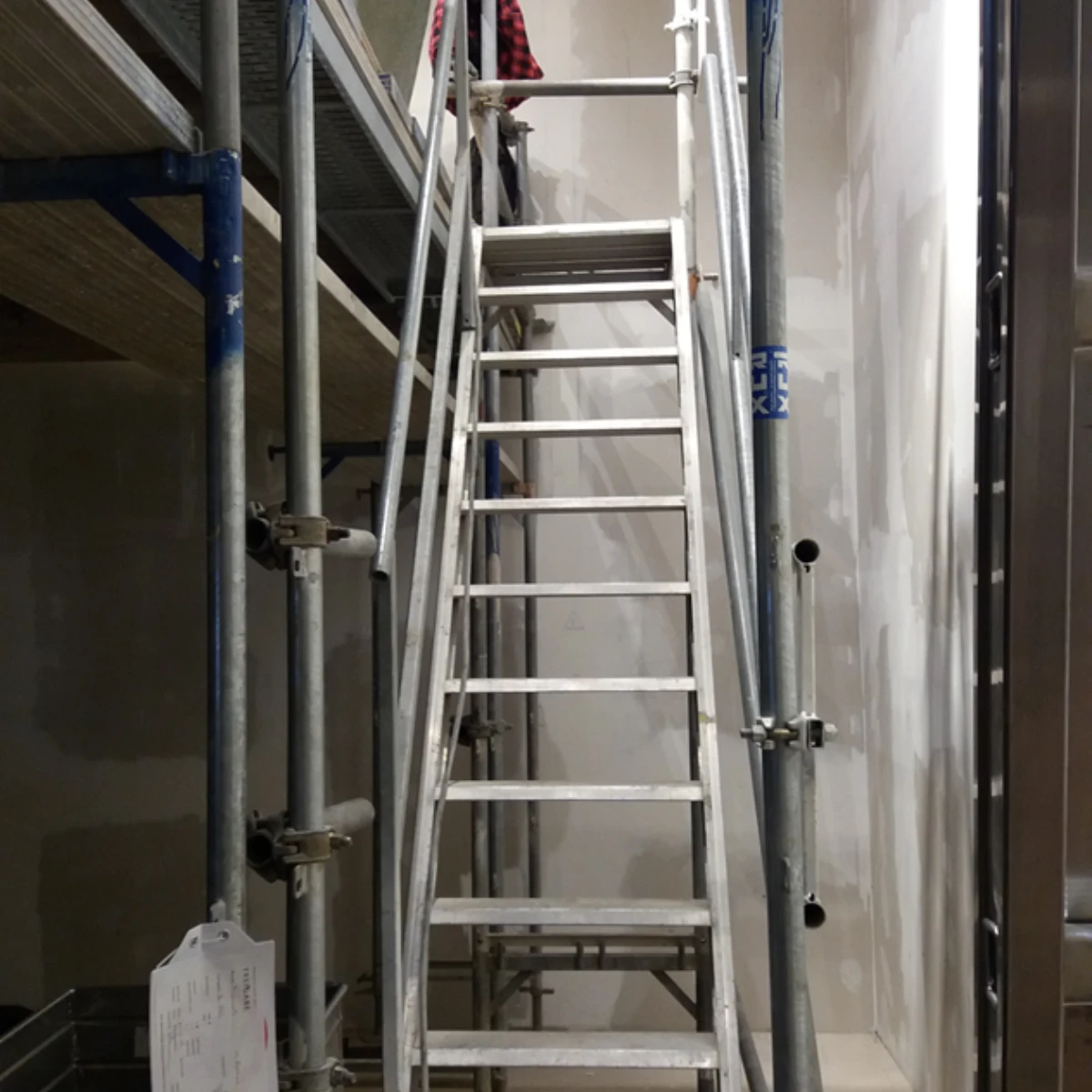 Leiter nach oben Scholz Maler Gerüstaufbau in einem Treppenhaus oder schmalen Gang, mit Leiter und frisch bearbeiteten Wandflächen.