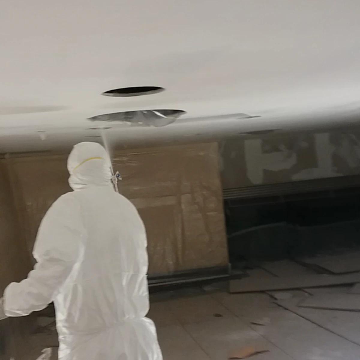 Maler im weißen Maler im weißen Schutzanzug trägt Farbe auf eine große Deckenfläche eines Innenraums auf.