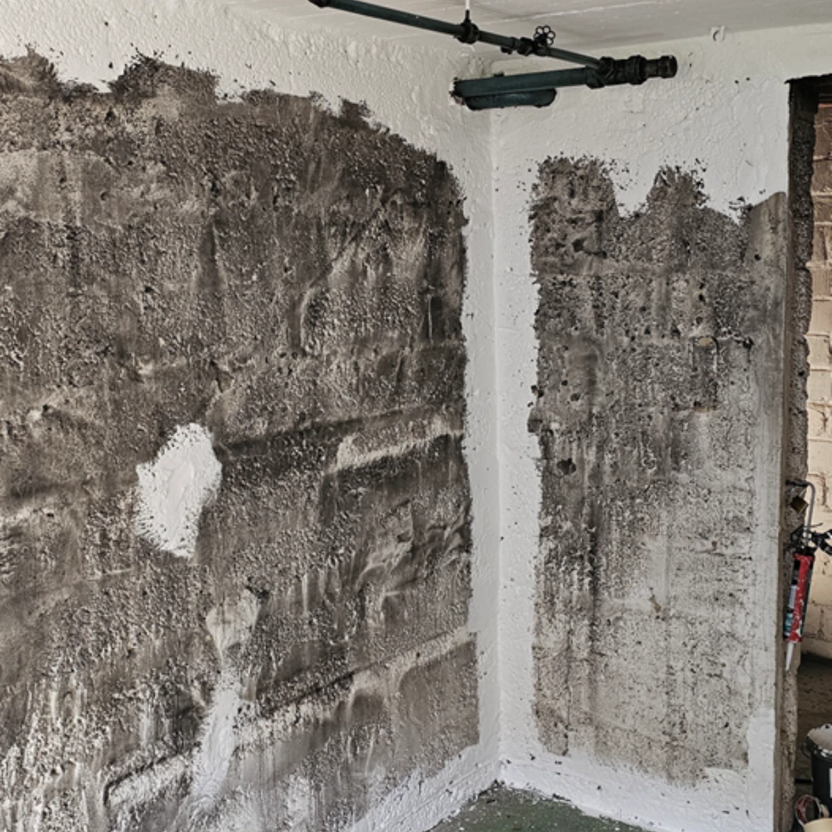 Kellerwand vorher Stark verrußte Kellerwand nach Brand, noch vor der Reinigung und Sanierung, mit sichtbaren Rauch- und Rußschäden.