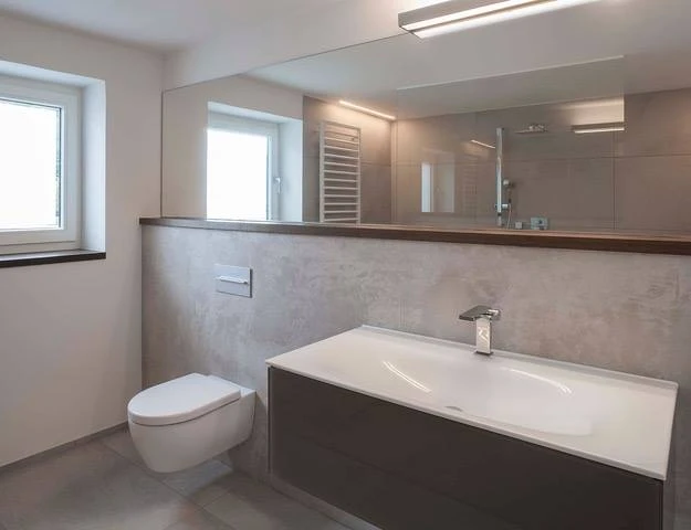 Renovierungsarbeiten innen Maler Scholz 3 Modernes Badezimmer mit Badewanne, wandhängendem WC und großem Spiegel, realisiert in hellen Naturtönen.